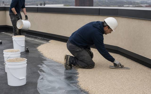 Installer in a hard hat spreading tan rubber surfacing across a rooftop terrace
