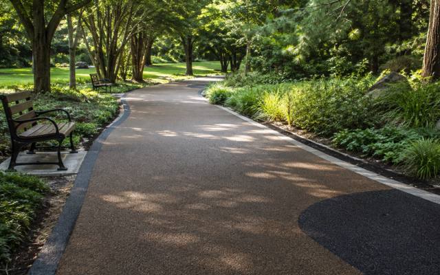 Brown rubber surfaced path curving through a park with a bench and trees