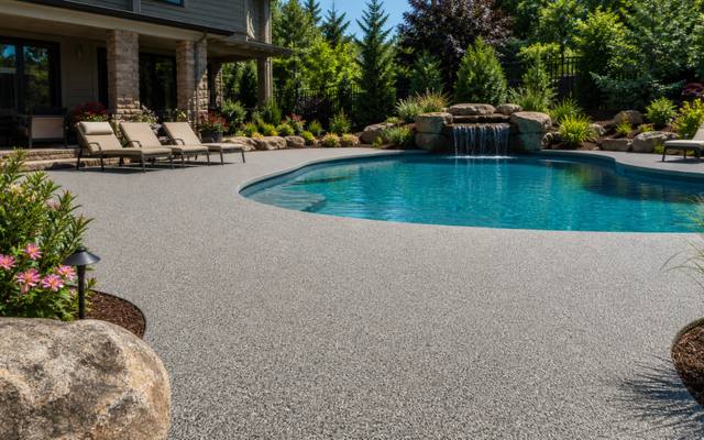 Backyard pool deck finished in tan rubber surfacing with lounge chairs and an umbrella