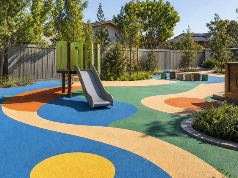 Daycare play area in blue, yellow and green rubber surfacing with a slide and planters
